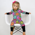 Child wearing a colorful checkered outfit with smiley face patterns on a white chair.