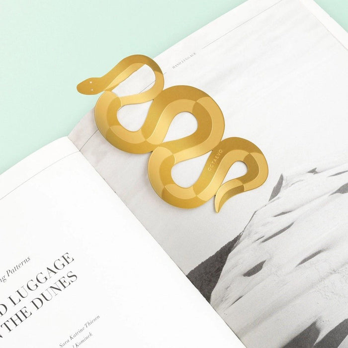 Brass snake bookmark in the middle of a book on a teal surface